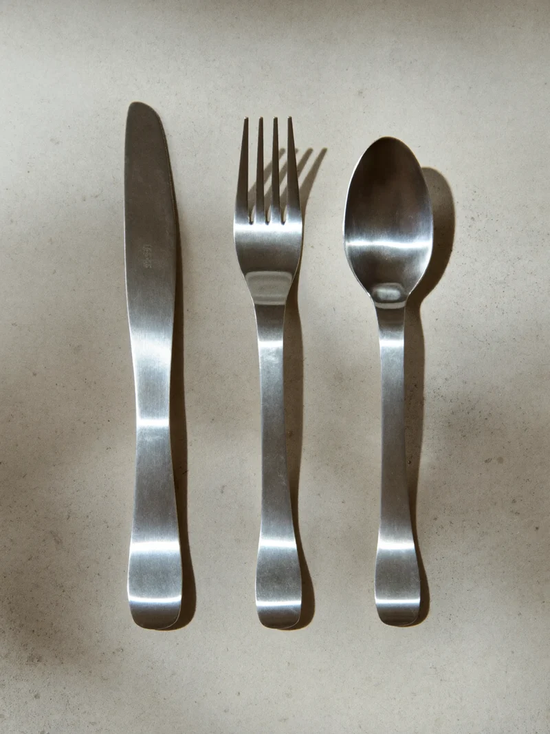 Couteau, fourchette et cuillère en acier satiné alignés sur une surface de pierre claire.