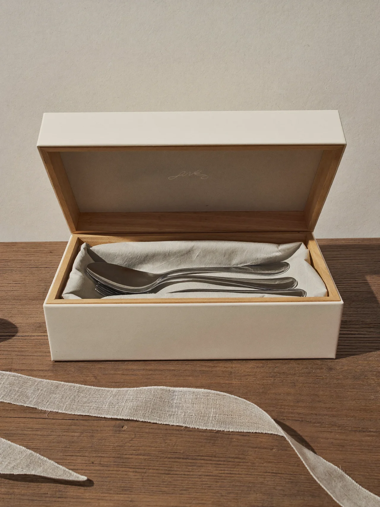 Coffret cadeau crème ouvert sur un service de couverts enveloppé de papier de soie.